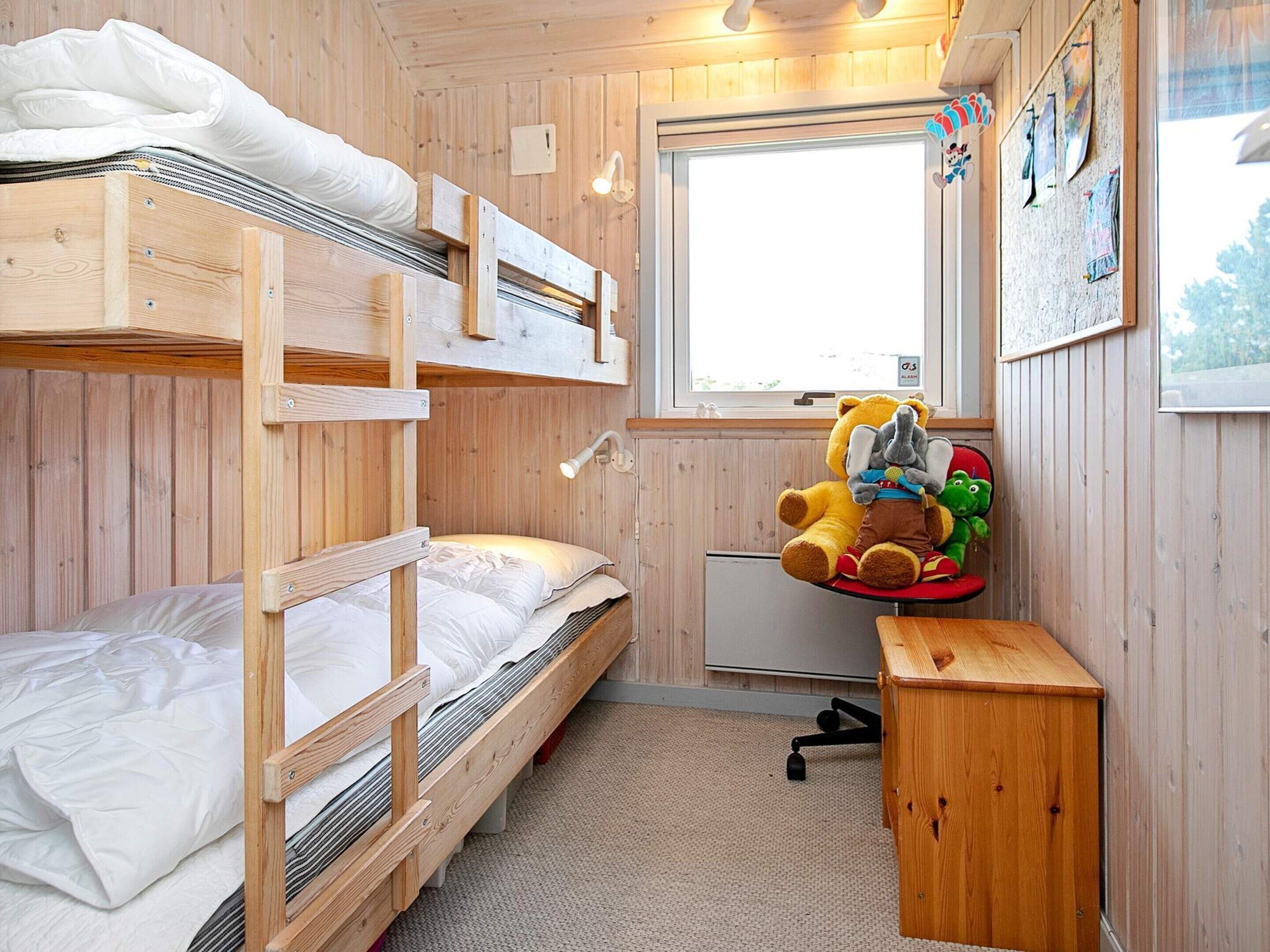 A bunk bed room with a desk and chair, a window, and a teddy bear.