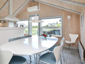 A modern kitchen with a white table and chairs, a hanging light fixture, and a view of the outdoors.