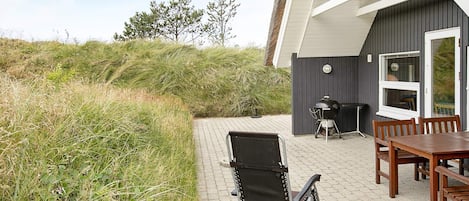 A patio with a table and chairs, a grill, and a folding chair.