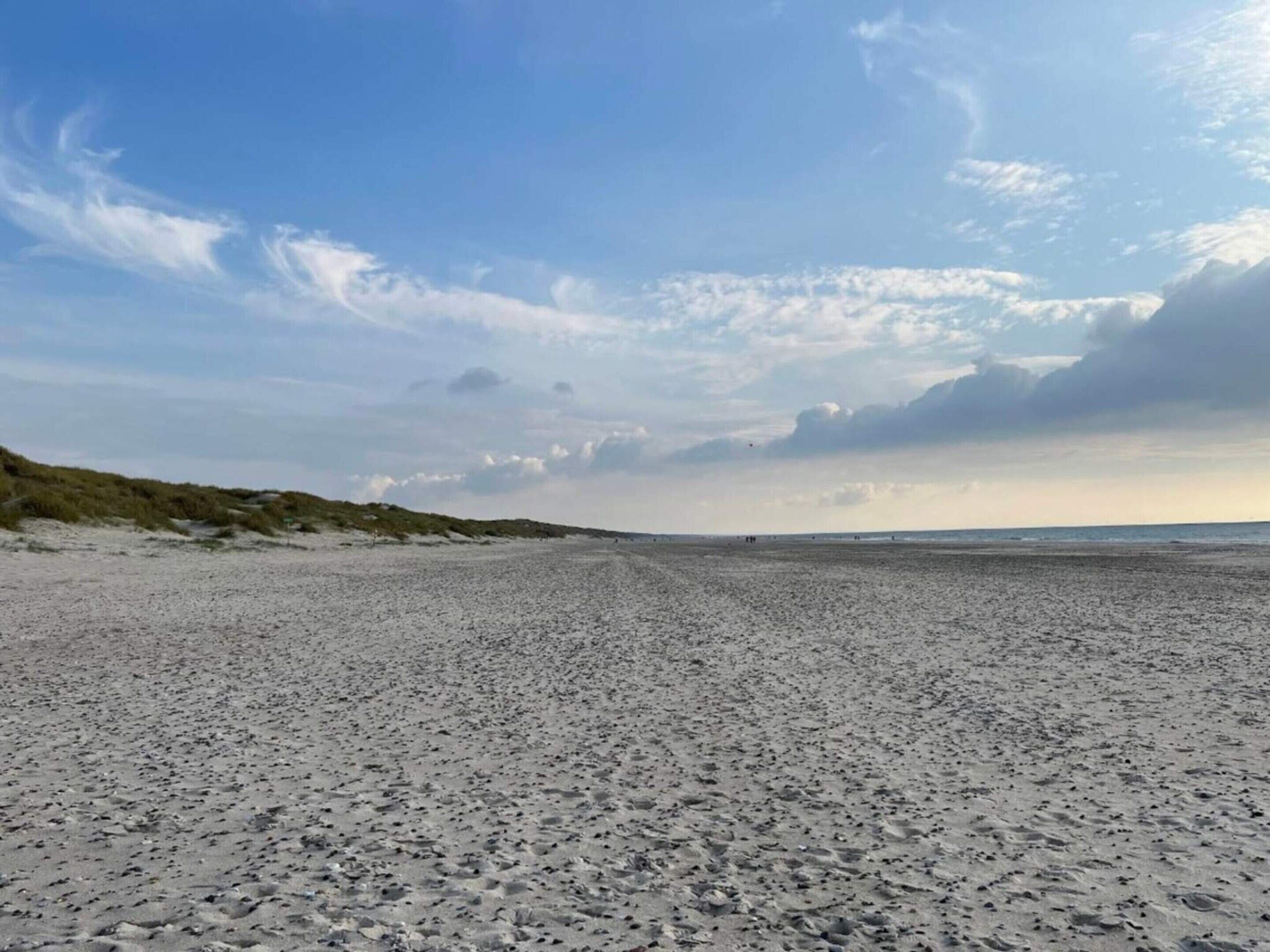 A wide sandy beach with dunes on the left and a clear sky above.