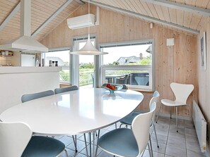 Une cuisine moderne avec une table et des chaises blanches, un luminaire suspendu et de grandes fenĂȘtres.