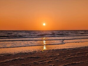 A sunset over the ocean with waves approaching the shore.