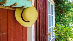 Eine hölzerne Veranda mit einem gelben Hut, der an einem Holzpfosten hängt, einem blauen Handtuch und einem Fenster mit weißem Zierrahmen.