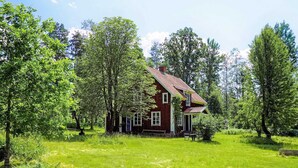 Ein rotes Holzhaus mit geneigtem Dach, umgeben von üppigen grünen Bäumen und Gras.