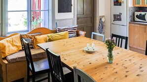 Ein gemütlicher Essbereich mit einem Holztisch, schwarzen Stühlen und einer Bank mit Kissen. Auf dem Tisch steht eine Vase mit Blumen.