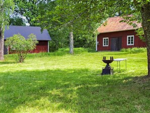 A red wooden house with a dark roof, surrounded by lush green grass and trees. - 7 Person Holiday Home in Odensbacken (Odensbacken)
