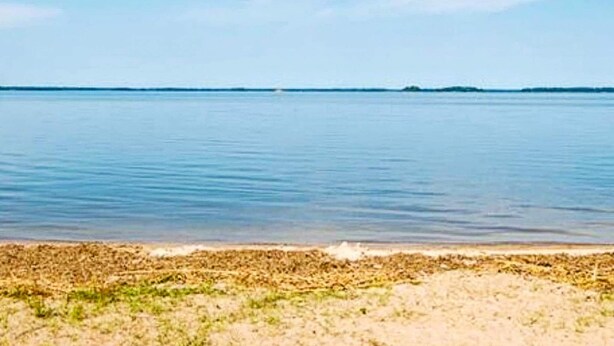 Ein Strand mit ruhigem Wasser und blauem Himmel.