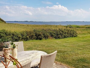 A table and chairs on a deck with a view of a body of water and distant land. - Holiday Home in Snedsted (Snedsted)
