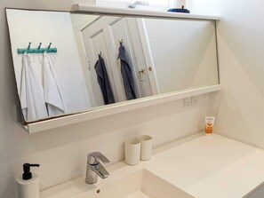 Un bagno con uno specchio grande, un lavandino bianco, un rubinetto e un porta asciugamani con degli asciugamani.