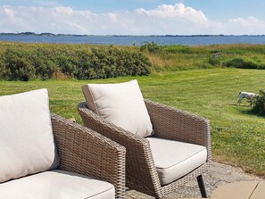 Wicker chairs with cushions on a patio overlooking a grassy area with a dog. - Holiday Home in Snedsted (Snedsted)