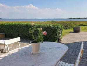 A patio with a marble table, a bench, and a potted plant with pink flowers. - Holiday Home in Snedsted (Snedsted)