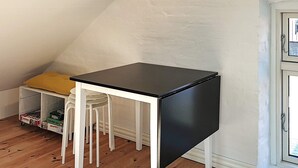 A small, white and black table with four chairs in a corner of a room with wooden flooring and a white wall. - Holiday Home in Snedsted (Snedsted)
