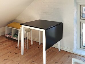 Una pequeña mesa blanca y negra con cuatro sillas en un rincón de una habitación con piso de madera y pared blanca.
