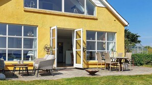 A yellow house with large windows, a patio with outdoor furniture, and a greenhouse in the background. - Holiday Home in Snedsted (Snedsted)