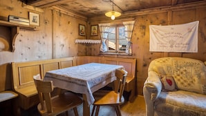 Een houten interieur met een tafel, stoelen, een bank, een raam met gordijnen en een muur met een lijst en een handdoek.