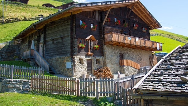 Een klassiek houten chalet met een stenen fundering, houten balkons en een stenen trap naar de ingang.