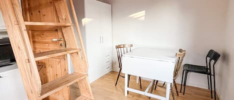 A wooden ladder, a white table, and two chairs in a room with wooden flooring and white walls.