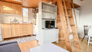 A modern kitchen with wooden cabinets, a white countertop, and a built-in TV. A wooden ladder is leaning against the wall, and a white table is in the foreground. - 4 Person Holiday Home in Fotö, Västra Götaland (Fotö)