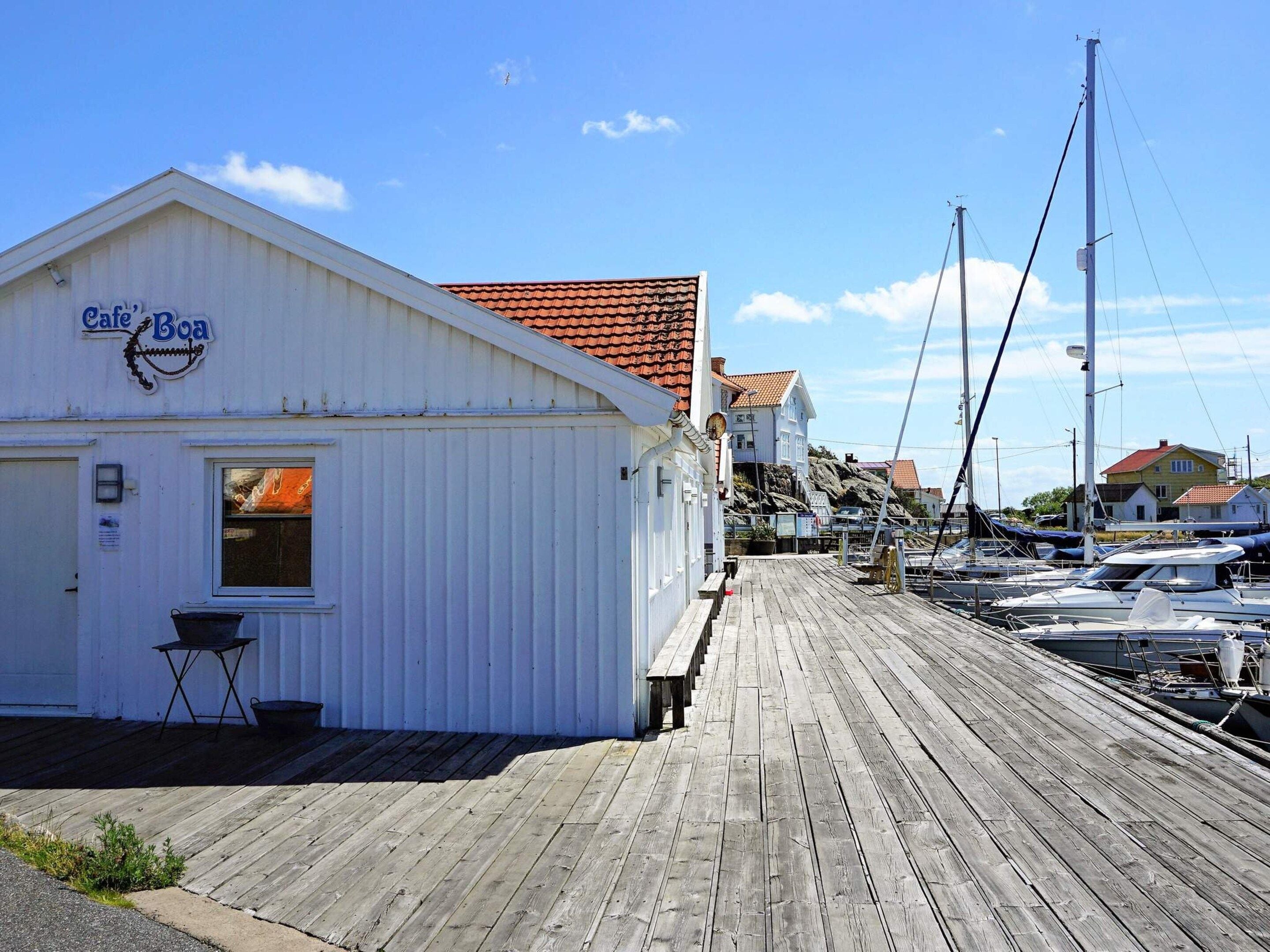 Un edificio blanco con un letrero que dice 'Cafe Boa' en un muelle de madera, con barcos amarrados al fondo.