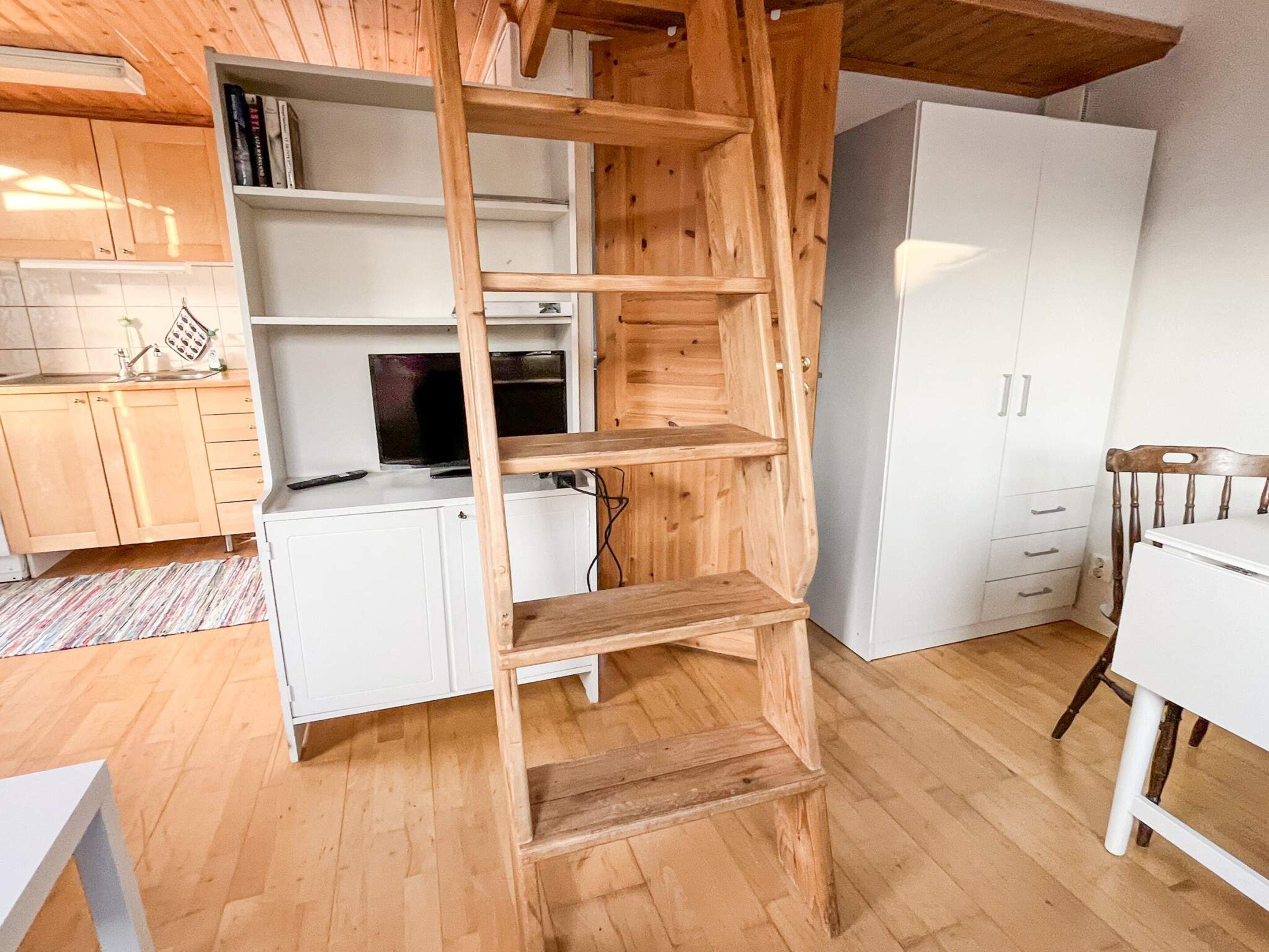 Una cocina con armarios blancos, un estante de madera en forma de escalera, un refrigerador blanco y una mesa de comedor de madera.