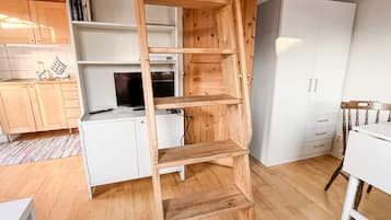 Una cocina con armarios blancos, un estante de madera en forma de escalera, un refrigerador blanco y una mesa de comedor de madera.