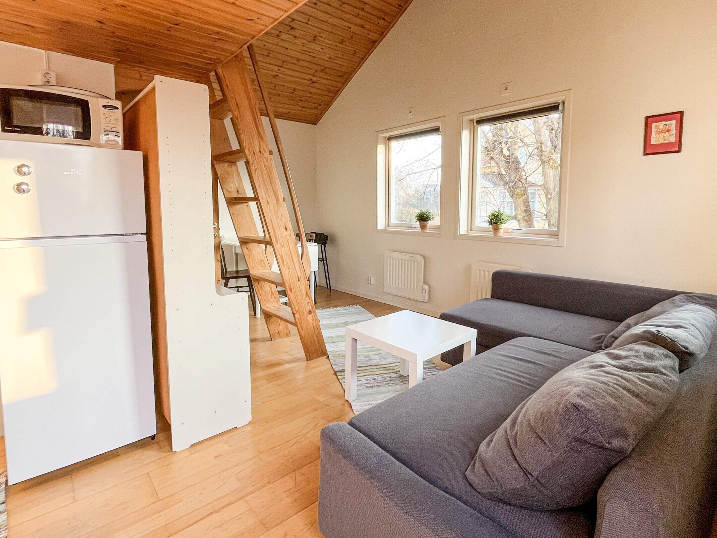 A compact living space with a kitchenette, a gray sofa, a white coffee table, and a wooden ladder.