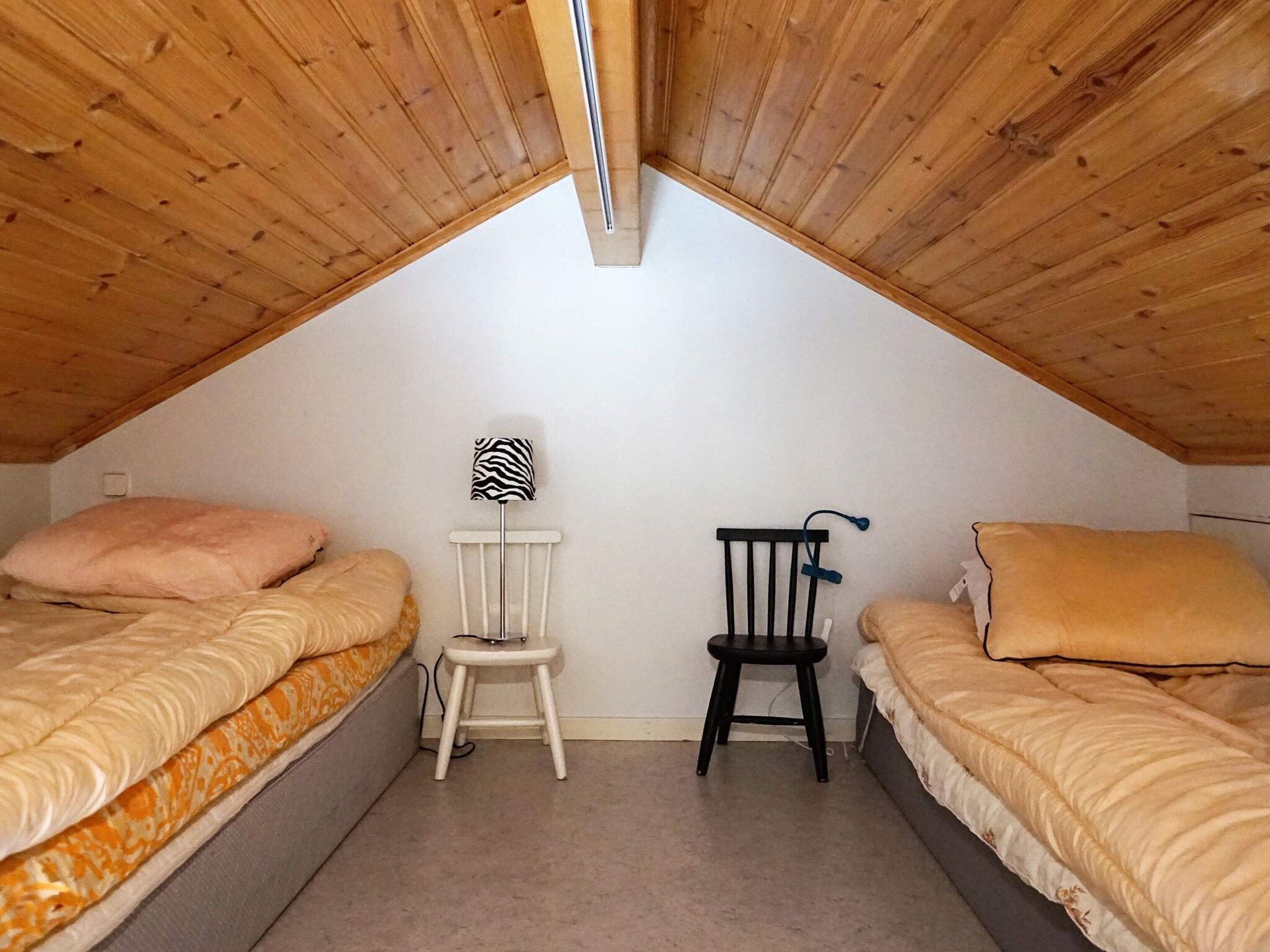 Un dormitorio ático pequeño con dos camas, una silla y una lámpara.
