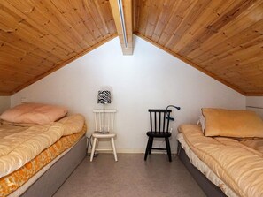 Ein kleines Schlafzimmer im Dachgeschoss mit zwei Betten, einem Sessel und einer Lampe.