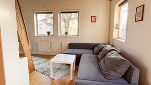 A cozy living room with a gray sofa, a small white table, and two windows with potted plants. - 4 Person Holiday Home in Fotö, Västra Götaland (Fotö)