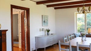 A dining area with a wooden table, white chairs, a grey cabinet, and a painting on the wall. - Holiday Home in LÃ¶derup (Loderup)