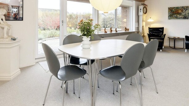 A modern dining area with a white table, grey chairs, a hanging light fixture, and a view through large windows. - 6 Person Holiday Home in Aeroskobing (Aeroskobing)