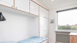 A bedroom with a single bed, white wardrobe, radiator, and a window with a view of buildings. - 6 Person Holiday Home in Aeroskobing (Aeroskobing)