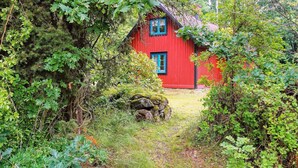 A red wooden house surrounded by dense greenery and a moss-covered stone wall. - 4 Person Holiday Home in Jamjo (Jämjö)