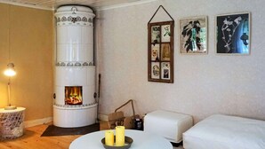 A cozy living room with a central fireplace, a round white table with candles, a white sofa, and framed pictures on the wall. - 4 Person Holiday Home in Jamjo (Jämjö)