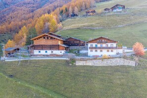 A rural mountain village with traditional wooden buildings, a stone wall, and a clear view of the surrounding hills.