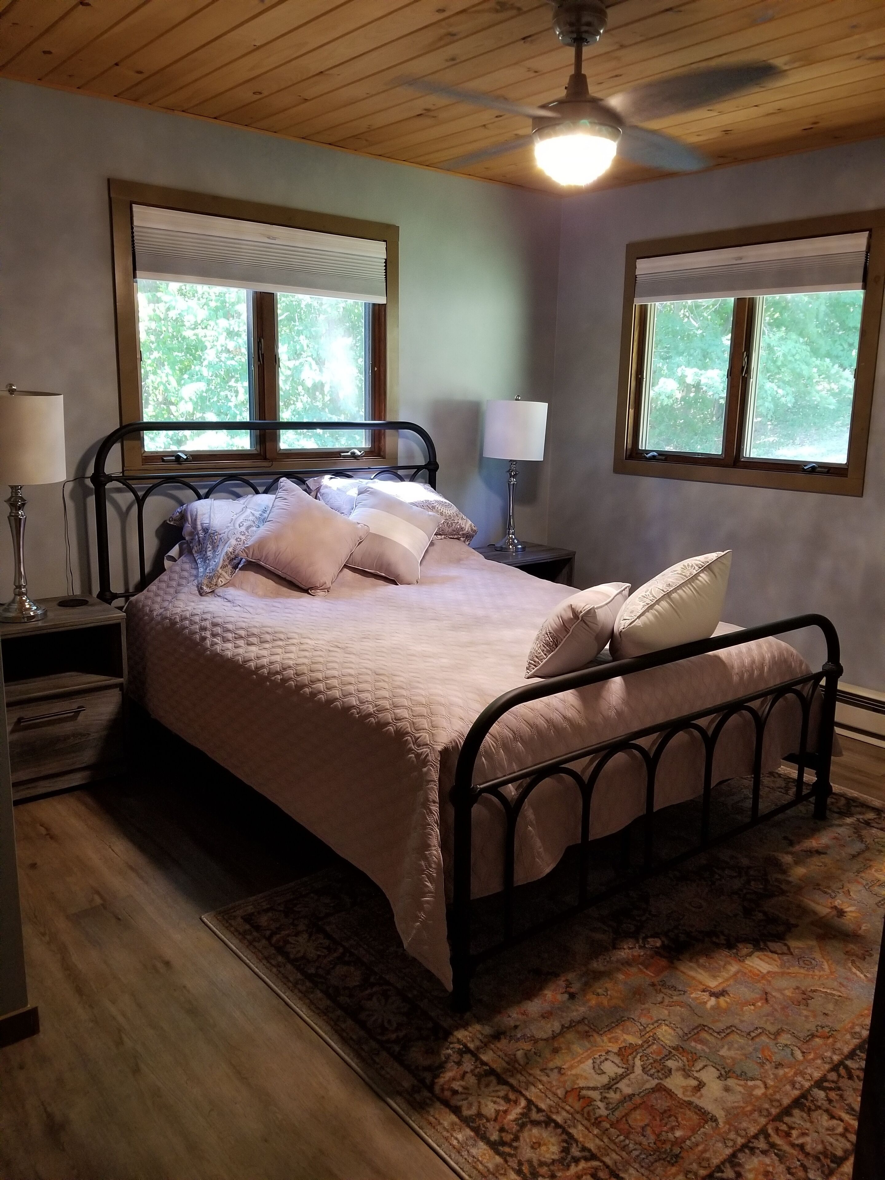 A bedroom with a bed, two bedside tables, a ceiling fan, and two windows with blinds.
