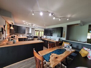A modern kitchen with dark cabinets, a central island, and a dining area with wooden chairs and a table.