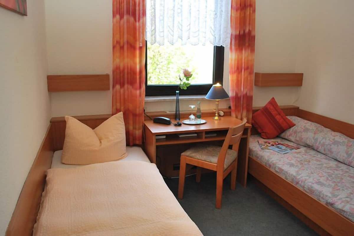 A small room with a bed, a desk with a chair, and a sofa.