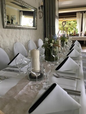 A long dining table set with white tablecloths, candles, and glassware, with a mirror and decorative items on the wall. - Hotel Waldschloss (Bad Camberg)