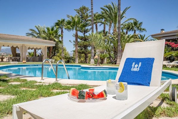 A poolside lounge with a clear view of the pool, surrounded by palm trees and a covered seating area.