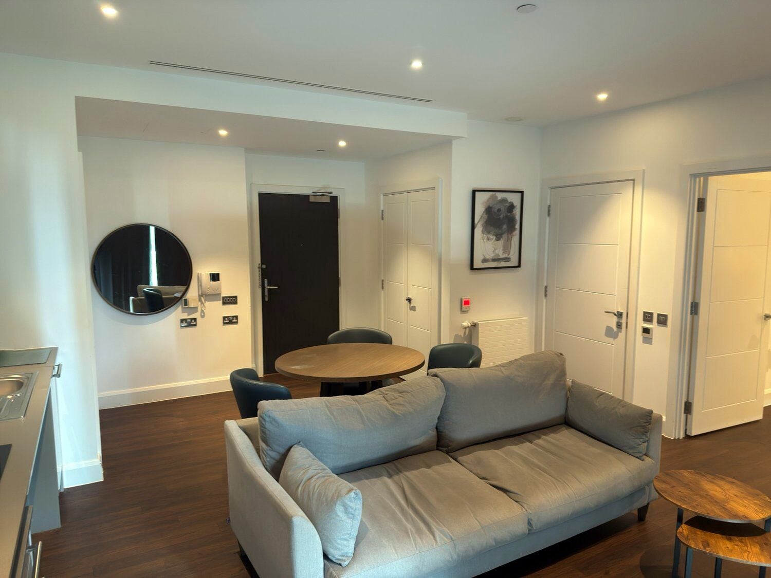 Uma sala de estar moderna com um sofá cinzento, uma mesa de madeira redonda e um espaço de jantar com cadeiras.