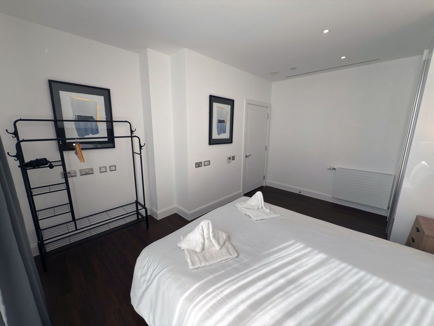 A hotel room with two beds, a black metal rack with clothes, and two framed pictures on the wall.