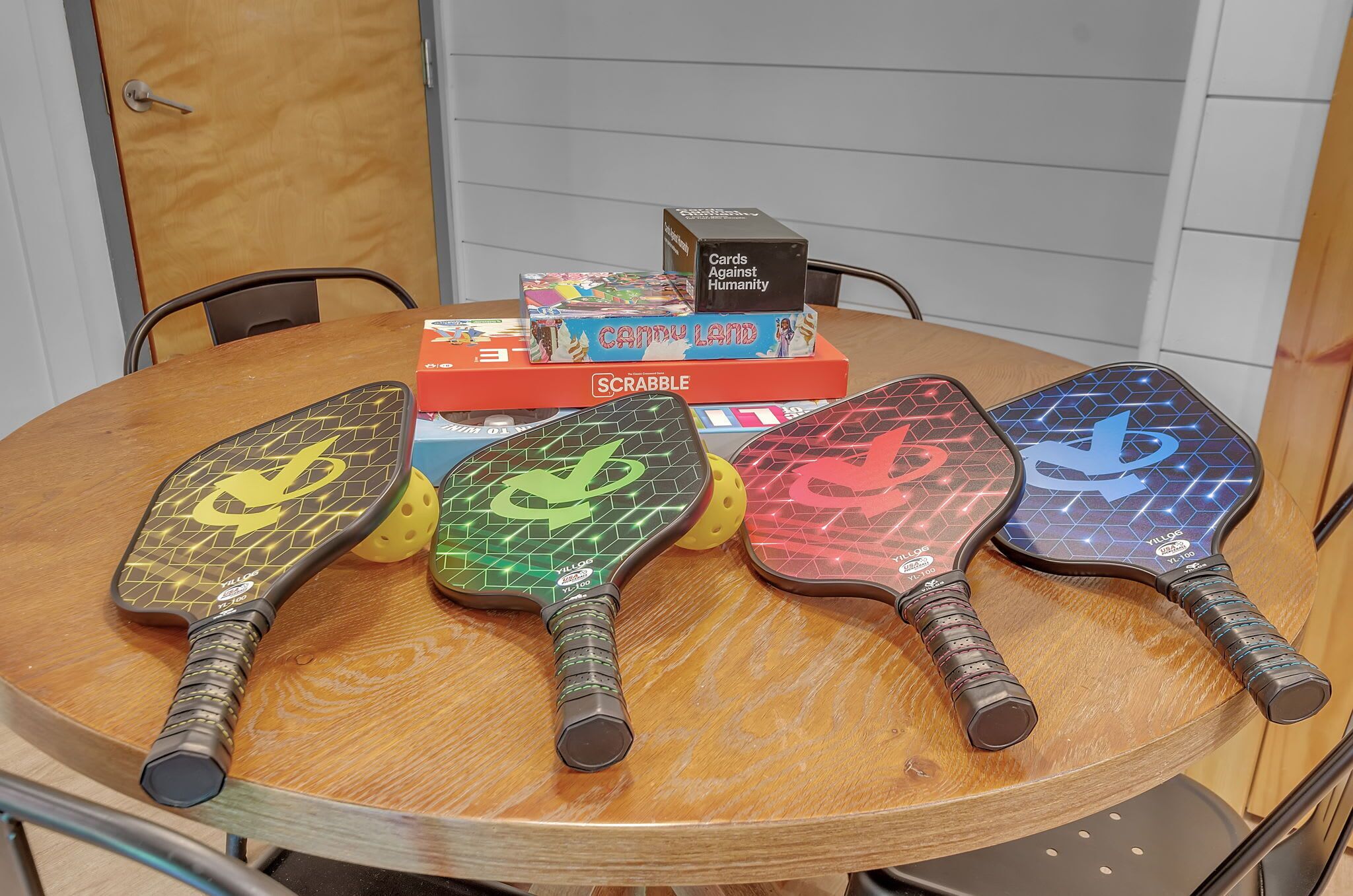 A table with a Scrabble box and five colorful paddle shuttles.