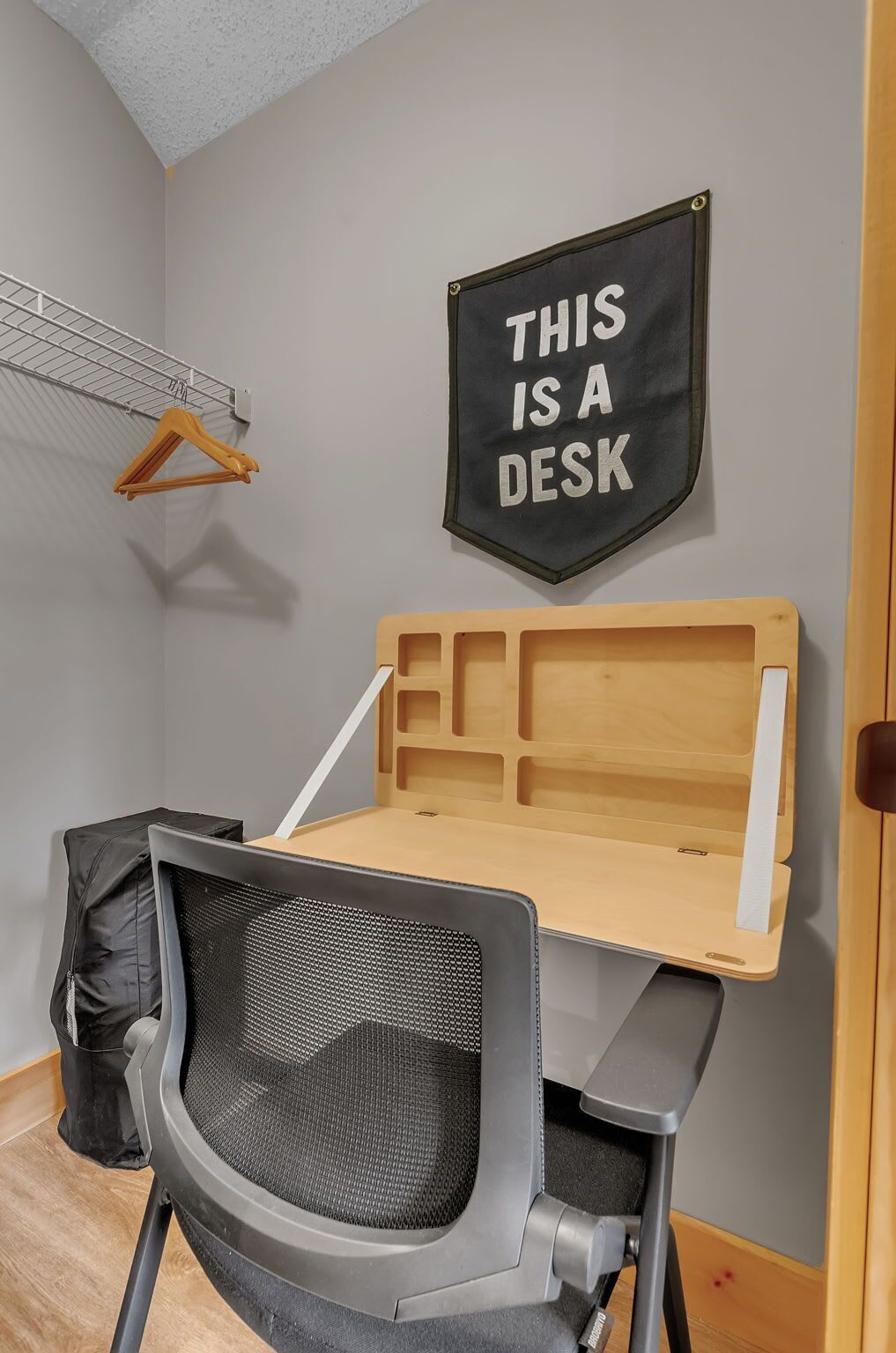 A compact workspace with a foldable desk, a mesh office chair, and a wall-mounted sign stating "THIS IS A DESK."