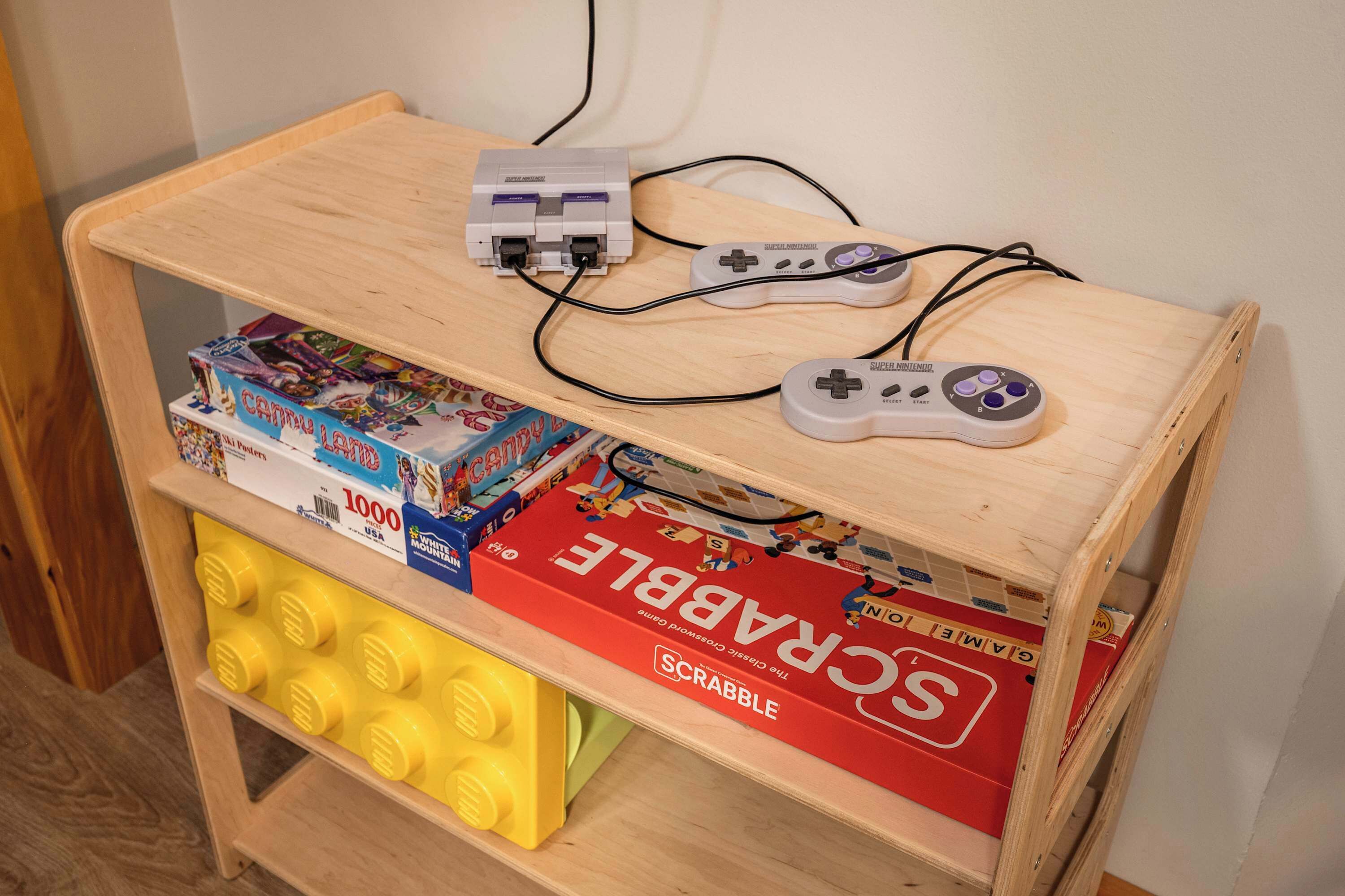 A wooden shelf with a Nintendo Switch console and controller, and several board games including Scrabble.