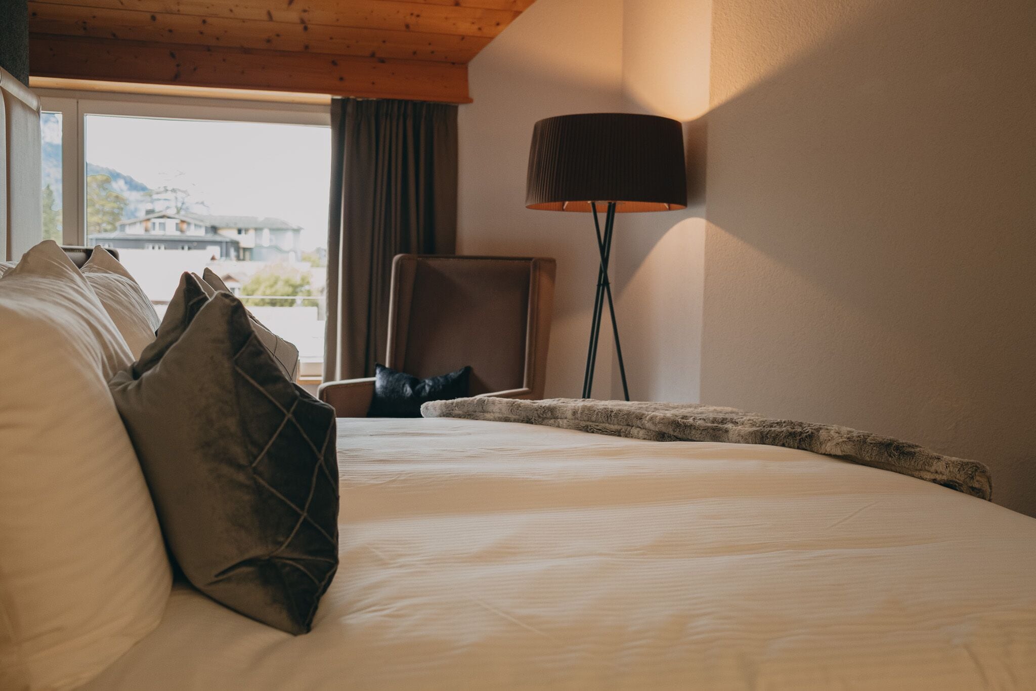 Ein Hotelzimmer mit einem großen Bett, einem Sessel, einer Lampe und Blick auf Gebäude.