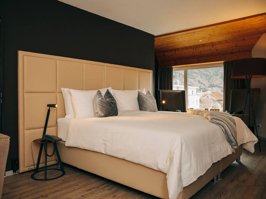 A bedroom with a large bed, a nightstand, a lamp, and a view of the outside.