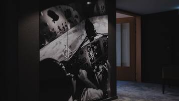A room with a large abstract painting on the wall, a door leading to another room, and a small table with a chair.