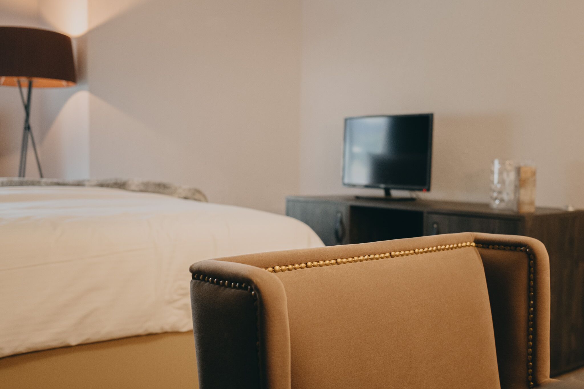 Una habitación de hotel con una cama, un televisor sobre un pedestal y una silla.