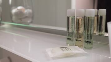 A bathroom counter with three bottles of Touch Concept hair and body care products, a small packet, and a glass jar in the background.